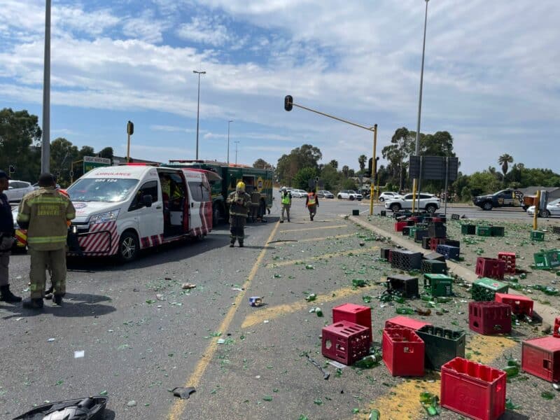 Emergency workers respond to a street accident with an ambulance and debris. Broken glass and colorful crates are scattered, conveying urgency and chaos.