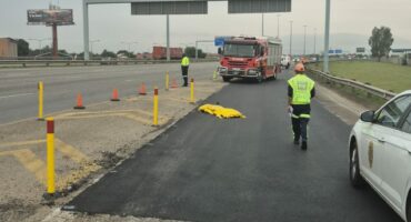 Emergency personnel manage a scene on a highway with a fire truck, traffic cones, and a covered object. Overcast sky and a calm, controlled atmosphere.