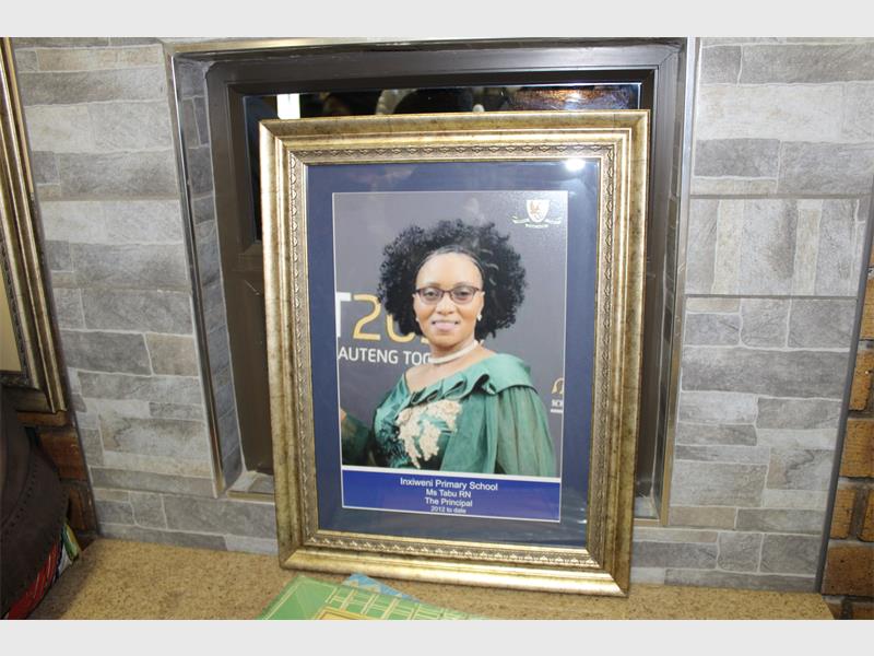 Framed portrait of a person in a green gown with a sash, set against a backdrop with text, placed on a stone mantel. Formal and celebratory tone.