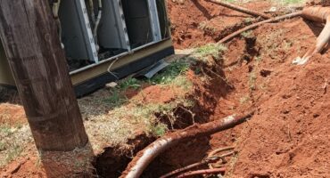 Underground cables exposed beside a utility box with open panels, surrounded by fresh red soil and dug trenches. The scene suggests ongoing repairs.