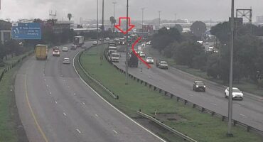 Highway scene in overcast weather with traffic congestion. Right lane blocked by a large vehicle marked by a red arrow, causing a backup.