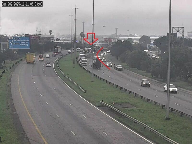 Highway scene in overcast weather with traffic congestion. Right lane blocked by a large vehicle marked by a red arrow, causing a backup.