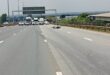 Wide highway with trucks and emergency vehicles blocking lanes ahead. A bike rests on the road surface. Overcast sky and a "Mr. Parking" sign visible.