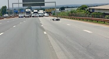 Wide highway with trucks and emergency vehicles blocking lanes ahead. A bike rests on the road surface. Overcast sky and a "Mr. Parking" sign visible.