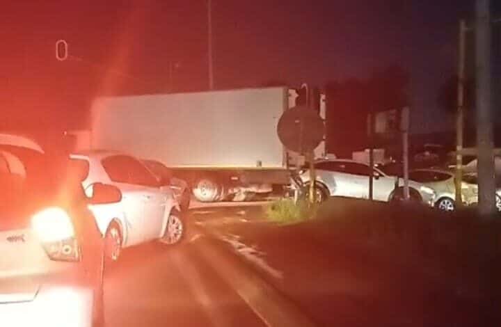 A nighttime traffic scene shows cars halted behind a truck blocking an intersection. Red taillights illuminate the road, conveying a tense and congested mood.
