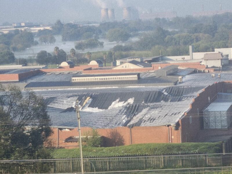 Aerial view of Festival Mall building complex with rusted metal roofs and brick walls. Background shows cooling towers and trees in a misty, rural setting.