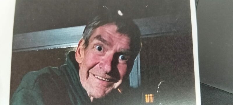 A person with wide eyes and a surprised expression looks through a window at night. Their face is illuminated, creating a mysterious, playful tone.