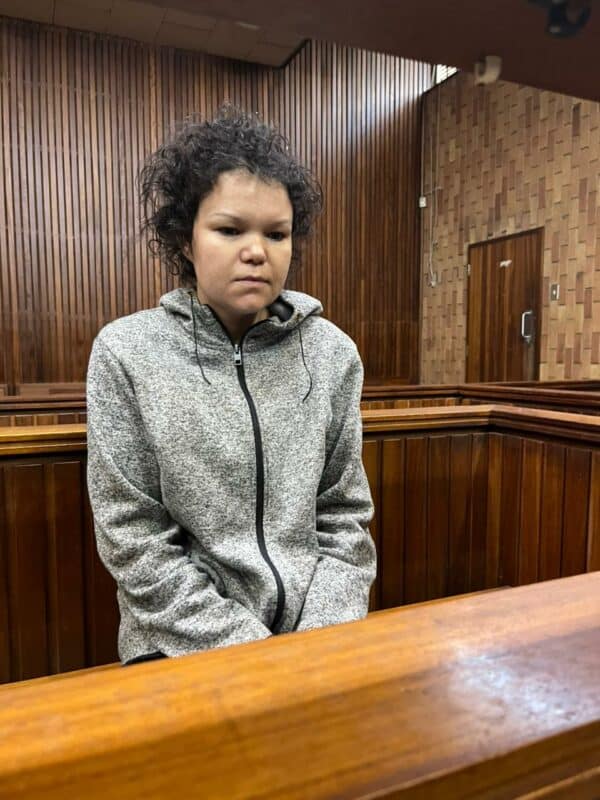 A person sits in a wooden courtroom, appearing concerned and pensive. They wear a grey hoodie, with wood paneling visible in the background.