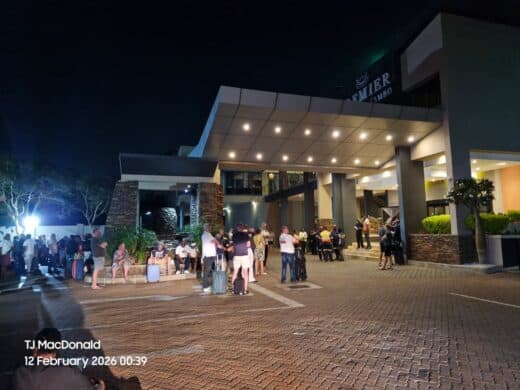 A nighttime scene shows a group of people with luggage gathered under a hotel entrance with bright lights. The mood is busy and expectant.