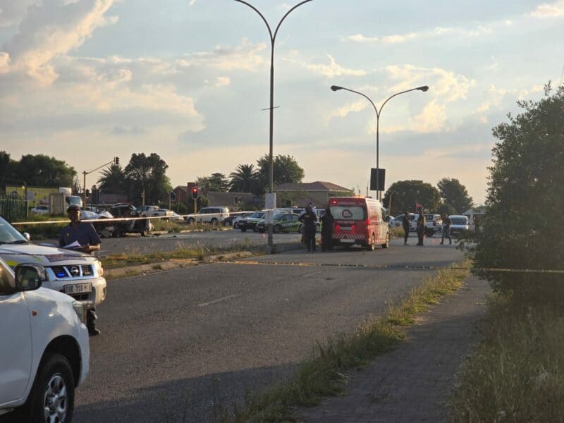 Police officers and emergency vehicles at a blocked urban street during sunset, marked with caution tape. Sky is partly cloudy and atmosphere is serious.