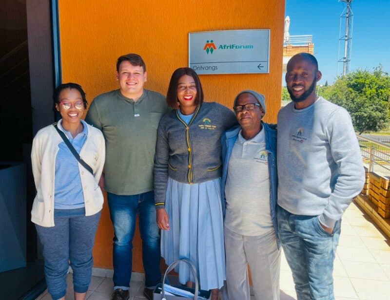 A diverse group of five people smiling outside a building with an