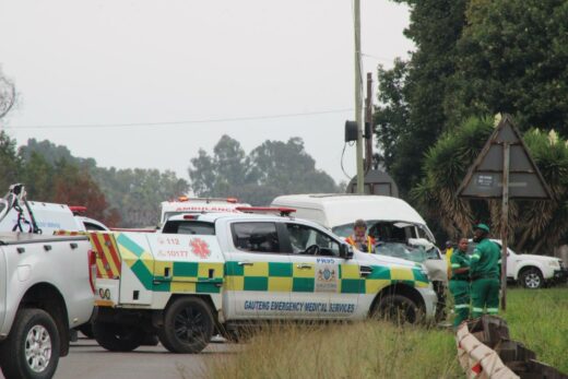 Emergency vehicles and personnel at a roadside scene. An ambulance and medical services truck are parked, with responders in green uniforms nearby.