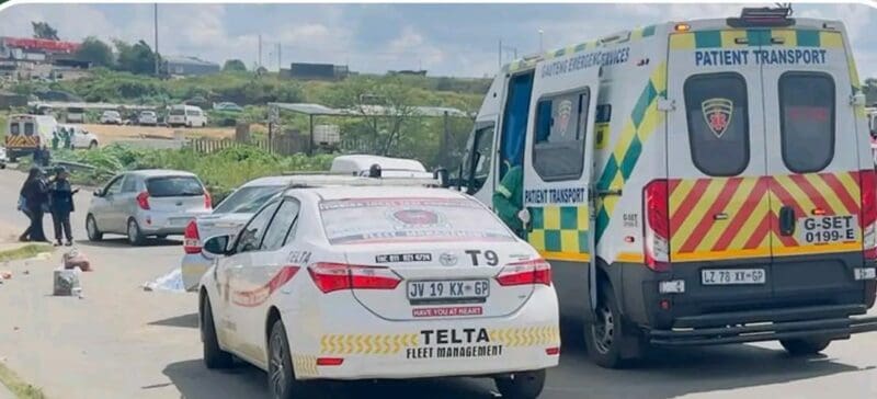 Ambulance and private security car on a road, with two people in uniform conversing nearby. The scene is set in a semi-rural area under a partly cloudy sky.