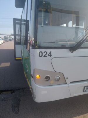 A white and green bus numbered 024 is parked on a road, with its door open. The bus is surrounded by vehicles under a clear sky.