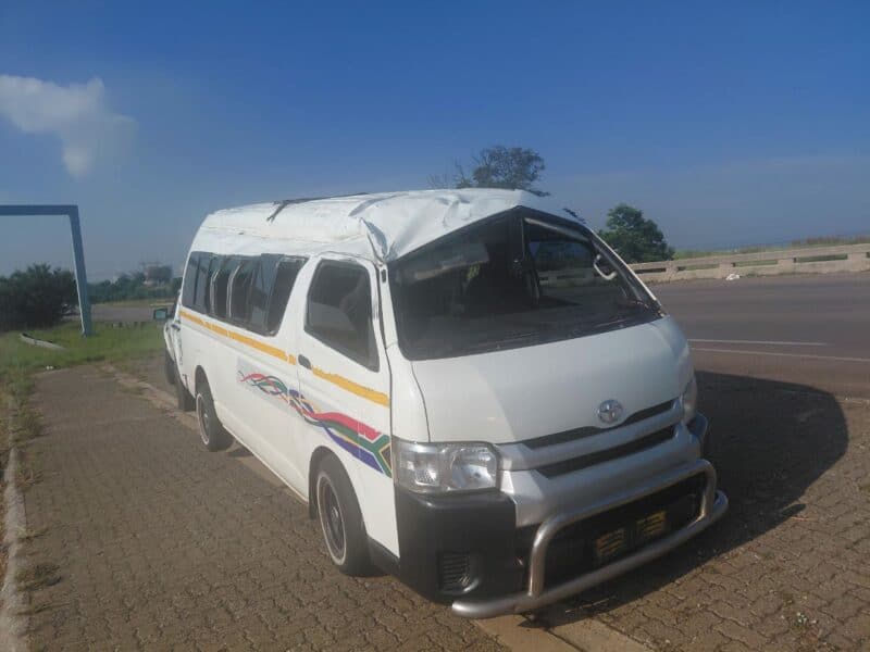 A white van with significant roof damage is parked on a roadside. The vehicle has colorful stripes along the side. The sky is clear and blue.