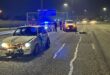 Damaged cars on a dimly lit highway at night, with police vehicles flashing blue lights. Officers and debris visible, conveying urgency and aftermath of a crash.