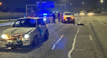 Damaged cars on a dimly lit highway at night, with police vehicles flashing blue lights. Officers and debris visible, conveying urgency and aftermath of a crash.