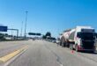 Traffic scene on a highway under a clear blue sky, with a line of trucks and cars stopped to the right, and a sign showing directions to Pretoria.