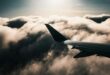 Airplane wing above dramatic, cloudy sky with sun setting, casting a serene, warm glow through the clouds. The mood is peaceful and contemplative.