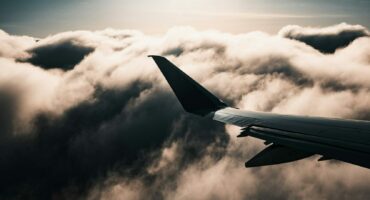 Airplane wing above dramatic, cloudy sky with sun setting, casting a serene, warm glow through the clouds. The mood is peaceful and contemplative.