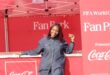 A smiling woman poses at a FIFA World Cup Fan Park event, showcasing a vibrant red backdrop with Coca-Cola branding.