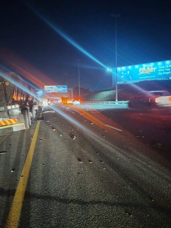 Nighttime highway scene with trucks, cars, streetlights, and billboards, featuring light streaks from vehicle headlights and lens flares.