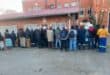 A diverse group of people waiting in line outside a brick building, showcasing community interaction in an urban setting.