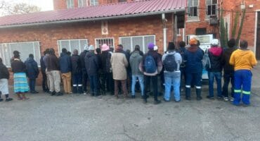 A diverse group of people waiting in line outside a brick building, showcasing community interaction in an urban setting.