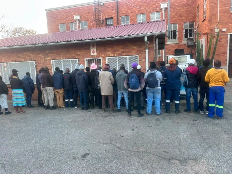 A diverse group of people waiting in line outside a brick building, showcasing community interaction in an urban setting.