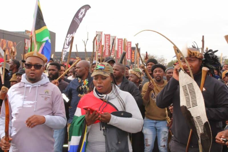 A diverse group of protesters holding signs and sticks during a demonstration, advocating for peace and social justice.