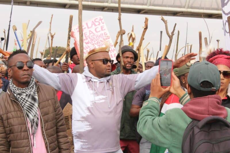 A diverse group of protesters holding signs and sticks during a demonstration, advocating for peace and social justice.