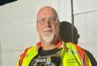 A community policing officer in a reflective safety vest stands confidently, showcasing his gear and commitment to safety and service.