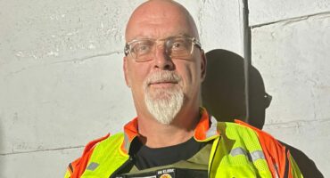 A community policing officer in a reflective safety vest stands confidently, showcasing his gear and commitment to safety and service.