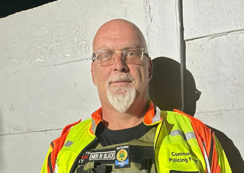 A community policing officer in a reflective safety vest stands confidently, showcasing his gear and commitment to safety and service.