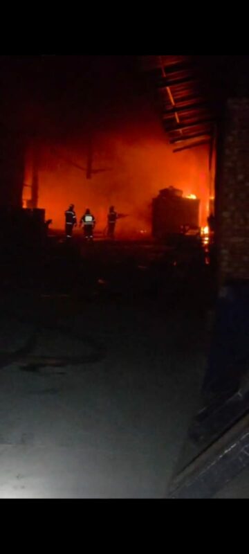 Firefighters battling a large blaze in a warehouse, with intense flames and smoke filling the scene during nighttime operations.