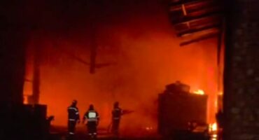 Firefighters battling a large blaze in a warehouse, with intense flames and smoke filling the scene during nighttime operations.