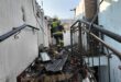 A firefighter in uniform inspects a damaged interior with debris and charred materials after a fire incident.