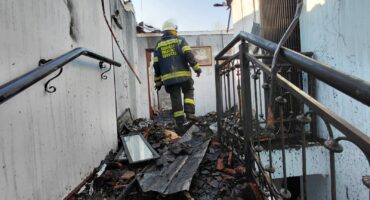A firefighter in uniform inspects a damaged interior with debris and charred materials after a fire incident.