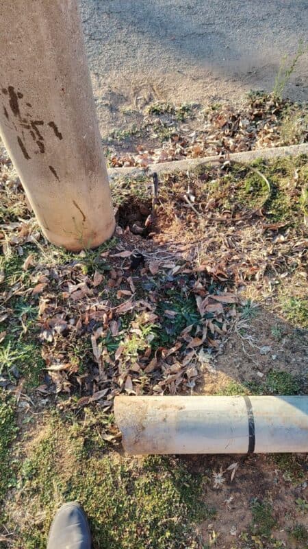 A concrete pole beside a dirt path, with a broken gray pipe lying on the ground and scattered dry leaves around.