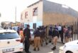 A group of EMPD officers in uniform stand outside a building with a metal fence, while white police vehicles are parked on the street nearby.