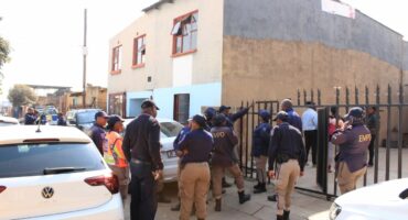 A group of EMPD officers in uniform stand outside a building with a metal fence, while white police vehicles are parked on the street nearby.