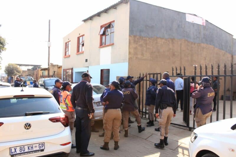 A group of EMPD officers in uniform stand outside a building with a metal fence, while white police vehicles are parked on the street nearby.