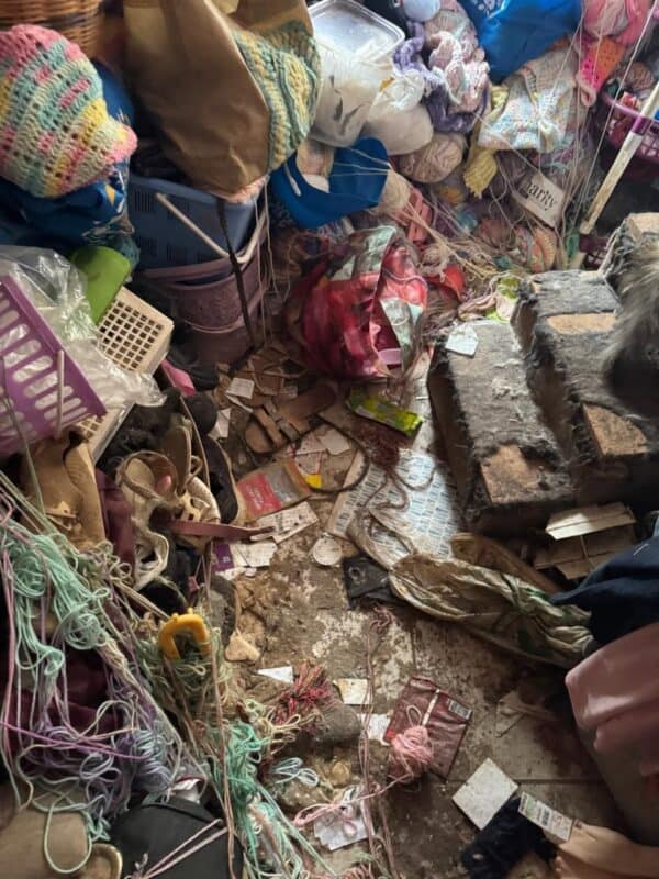 A cramped, cluttered craft stall filled with colorful yarn, woven baskets, textiles, tools, and debris, creating a crowded, handmade atmosphere.