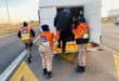 EMPD officers in orange safety vests help a bundled traveler into a white truck on a highway shoulder, creating a cooperative scene.