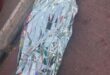 Person-shaped figure wrapped in a reflective silver emergency blanket lies beside a curb on a brick sidewalk, creating a somber, urgent scene.