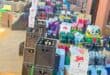 Colorful beverage crates and boxes of beer, soda, and bottled drinks crowd a small storefront, creating a busy, vibrant market scene.