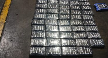 Rows of shiny rectangular blocks stamped “AIR” form a grid on a dark industrial floor beside a yellow safety line and blue device.