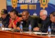 South African police officials sit at a press conference table beneath a SAPS Crime Stop banner, appearing serious and focused.