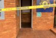 Brick police station entrance cordoned off with yellow SA Police Service tape; emblem, open doorway, and wheelchair sign create a tense scene.