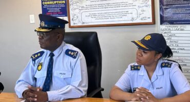 Two police officers sit at a wooden table beneath an anti-corruption pledge and code of conduct posters, conveying professionalism and integrity.
